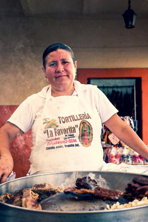 The photo shows a woman selling "tortas" (a typical Mexican dish) at a food market in Tequila, Jalisco.